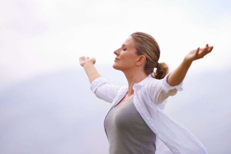 Woman standing outside with her head tilted toward Jesus and arms spread wide